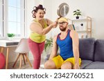 Small photo of Crazy plus size housewife having fun and hitting her husband with frying pan. Happy, funny, fat woman in hair curlers wants to fight and hits man on head with heavy skillet