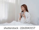 Small photo of Beautiful asian woman has woken up on a white bed and holding coffee in the morning at home. lifestyle concept.