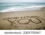 GOD LOVES YOU. Words written in beach sand. The words GOD LOVES YOU written in the sand on the beach with the ocean as the background. God's Love is all you need. Everyone Loves the beach. 
