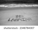 Small photo of # Lahaina. Lahaina Hawaii. The name # LAHAINA written in the sand on the beach with the Pacific Ocean background. Lahaina, Maui Hawaii. Hawaiian Tragedy. Sign in the Hawaiian Beach Sand. Black - White