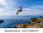 Small photo of Dubrovnik, Croatia - October 2022: Unidentifiable man ziplining above Dubrovnik old town; thrill seeking holiday adventure; extreme sport; panoramic view of the old town and Adriatic Sea