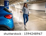 Woman in a parking garage, unlocking in her car. Woman activating her car alarm in an underground parking garage as she walks away. Business woman walking with car keys in the underground parking