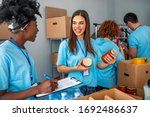 Small photo of Group of people working in charitable foundation. Happy volunteer looking at donation box on a sunny day. Happy volunteer separating donations stuffs. Volunteers sort donations during food drive