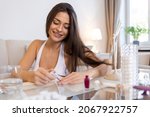 Young woman doing daily nail care routine at home. Portrait of happy young woman polishing nails with nail file lying on comfortable sofa at living room and looking at camera with smile. 