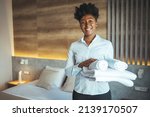 Small photo of Maid working at a hotel holding towels and looking at the camera smiling - housekeeping concepts. Maid with fresh clean towels during housekeeping in a hotel room