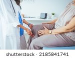 Small photo of Photo of senior woman having some knee pain. She's at doctor's office having medical examination by a male doctor. The doctor is touching the sensitive area and trying to determine the cause of pain.