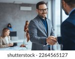 Small photo of Portrait of cheerful young manager handshake with new employee. Business partnership meeting in office. Close up of handshake in the office. Mature businessman shake hands with a younger colleague