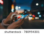Hand with a smart phone in a dark. Female using her mobile phone, city skyline night light background. Girl pointing finger on screen smart phone on background illumination color light in night city