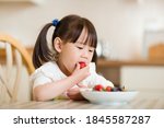 young girl eating strawberry against real kitchen background