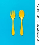 Small photo of Bright yellow plastic spoon and fork on a blue background. Plastic food set. Flat lay.