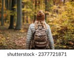 Woman with backpack hiking on footpath in autumn forest. Solo female tourist outdoors