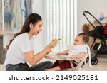 Small photo of Side view mother feeding her asian baby daughter with pumpkin mashed or vegetable mash on rubber spoon.Mom trying to feed little baby boy at home enjoy and spending time together.Baby feeding Concept