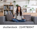 Clam of Asian young woman doing yoga lotus pose to meditation and relax on couch during work online at home.Happiness female break after worked close her eyes and deep breath with yoga so peaceful.