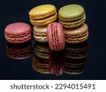 A group of delicious and colorful macarons are reflected on the glossy black support base