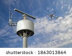 Rotating coastal radar surveillance station under the cloudy summer sky by the sea catching an airplane flying in the air space