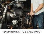 Small photo of rider install a motorcycle saddlebag or side bag on luggage bracket vintage motorbike. motorcycle travel concept. selective focus