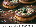 Pastries concept. Donuts with chocolate glaze with sprinkles, on wooden table blurry background.