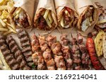 Small photo of Greek street food variety, gyro sliced meat pita bread wrap, chiken and pork souvlaki skewer. Wooden table, top view