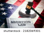 Abortion law in USA concept. Pregnancy termination ban. Judge gavel and Abortion Law book on US flag, close up view 
