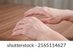 Small photo of Old woman trembling hands due to Parkinson disease. Lady with shakiness holds wrinkled hands over table. Elderly female hands tremor closeup
