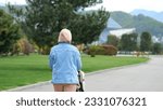 Small photo of Mother wearing denim jacket walks with baby cradle in amusement park past grass lawn. Woman wants child sleeping in cradle to breathe fresh air