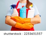 A woman in gloves and apron holding cleaning products on blue background
