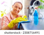 Housewife in yellow gloves wipes dust using spray detergent and rag