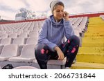 close up of young adult caucasian female sitting alone at the stadium, smiling, with headphones in her ears. handsfree cellphone conversation