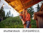 A young girl is enjoying the view from cottage porch in the forest on a beautiful evening. Vacation, nature, cottage