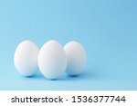 Three white chicken egg standing vertical on blue background with copy space.