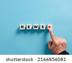 Small photo of Male hand presses the play button with the news on wooden cubes. Broadcasting, publishing or watching the latest news concept.