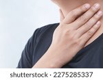 Small photo of sore throat pain. Closeup of young man sick holding her inflamed throat using hands to touch the ill neck in blue shirt on gray background. Medical and healthcare concept. Focus red on to show pain.
