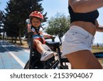 Portrait of little toddler boy with security helmet on the head sitting in bike seat and his mother with bicycle. Safe and child protection concept. Family and weekend activity trip