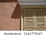 Small photo of Old Neoclassical house mellow ochre wooden window louvered shutters with a white plaster head on a salmon pink Venetian stucco wall.