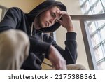 Small photo of upset tense young man in a hood, sitting on the stairs and looking away, experiencing problems and misunderstanding. Teenage transition age. The concept of loneliness. Close-up