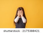 shy child who is ashamed of his bad behavior without showing his tears. a little girl covering her face with her hands is afraid of a horror movie on a yellow background. Body language