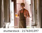 Small photo of A young man works in a brewery and checks the quality of craft beer. The brewery owner tastes the best beers from Bach. A man's shortcut fills a glass of beer with