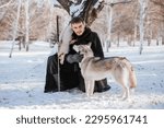a knight in a black cloak and in furs with a sword in his hand in a snowy forest. Young male warrior in winter with a wolf. A guy with a Siberian helmet. fantasy image