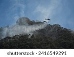 Small photo of BOGOTA,BOGOTA DC, COLOMBIA - 01232024 Helicopter carrying giant bucket of water to extinguish a fire in the mountain
