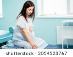Small photo of Caucasian pregnant woman with painful contraction sitting at hospital ward, touching belly and looking down. Childbirth process at hospital.