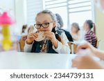 Small photo of Adorable schoolgirls wit Down syndrome taking lunch at school cafeteria. Integration of children with special needs concept.