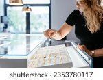 Attractive female jewelry seller standing behind counter put gold ring on a display at modern jewelry shop. Luxury jewelry store concept. Luxury jewelry store concept.
