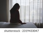 Small photo of Silhouette of a woman sitting and crying on a bed in bedroom