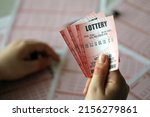 Small photo of Filling out a lottery ticket. A young woman holds the lottery ticket with complete row of numbers on the lottery blank sheets background. Gambling concept