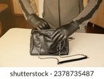 Small photo of Robber in black outfit and gloves see on opened stolen women bag. A thief evaluates the value of stolen items from a womans handbag in kitchen interior