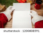 Santa Claus holding letter on wooden table with gift boxes and Christmas tree and cup of hot coffee or tea.  mockup blank