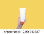 Small photo of Woman hand holding sunscreen tube over yellow background. Plastic bottle of SPF sunblock cream for protect against wrinkles, discoloration and skin cancer. Daily skincare products for sun protection.
