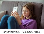 Small photo of Upset depressed caucasian little kid girl holds mobile phone expresses sorrow and regret blames