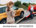 Elegant middle age business woman calling someone while towing service helping her on the road. Roadside assistance concept.	