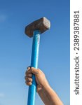 Small photo of Hammer in hand on sky background. Hit and destroy concept. Strong man's hands with a sledgehammer isolated on white.